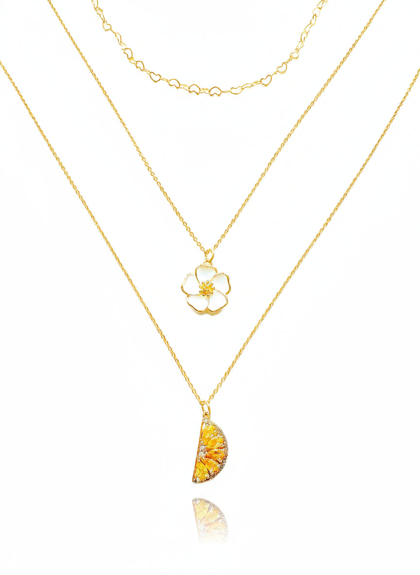 A stack of gold-filled necklaces, featuring a small gold-filled flower pendant on one of the chains, and a larger pendant with a yellowish-gold tone on another, against a white background.