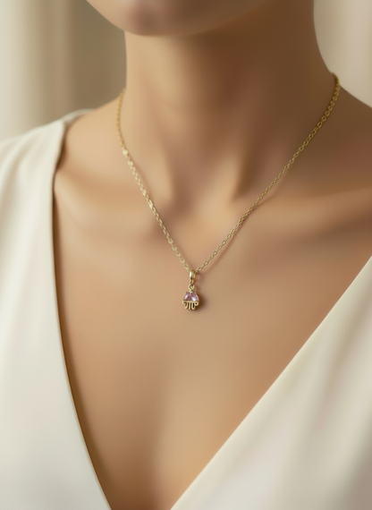 Gold necklace with a pink gemstone pendant on a mannequin wearing a white top.