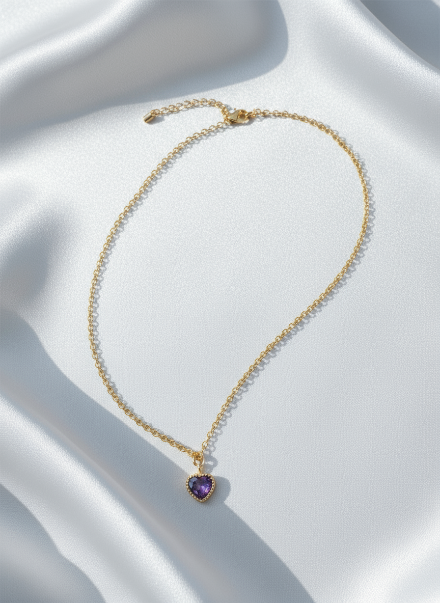 Gold necklace with a heart-shaped purple pendant on a white surface