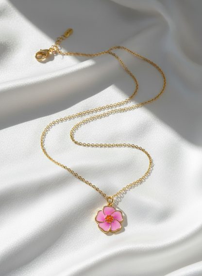 Gold necklace with a pink flower pendant on a white fabric background