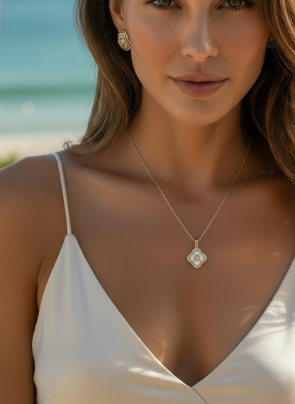 Woman wearing a gold necklace with a floral pendant on a beach.