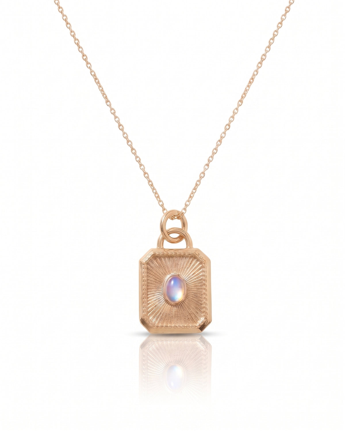 A rose gold pendant necklace featuring a textured, geometric rectangular box pendant with a central iridescent oval gemstone, suspended from a delicate chain on a white background with a soft reflection below.