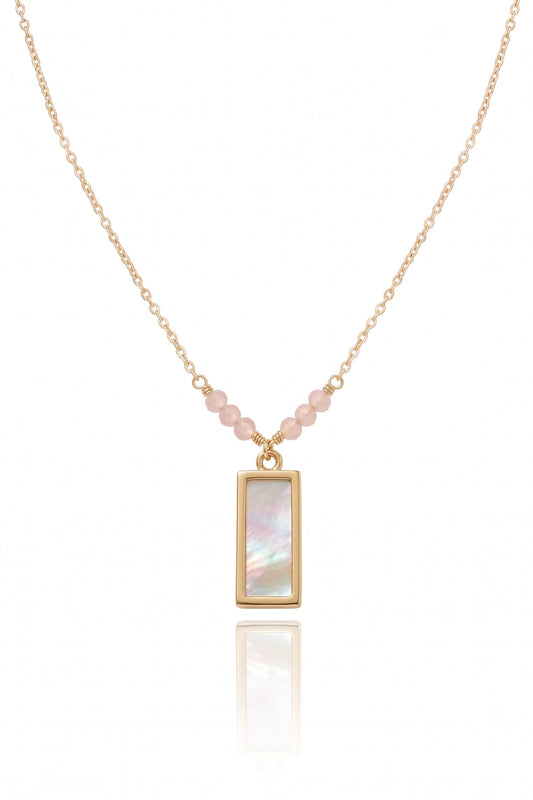 A delicate gold chain necklace featuring a vertical rectangular pendant with an iridescent mother-of-pearl inlay, accented by small pink beads along the chain, shown on a white background with a soft reflection.