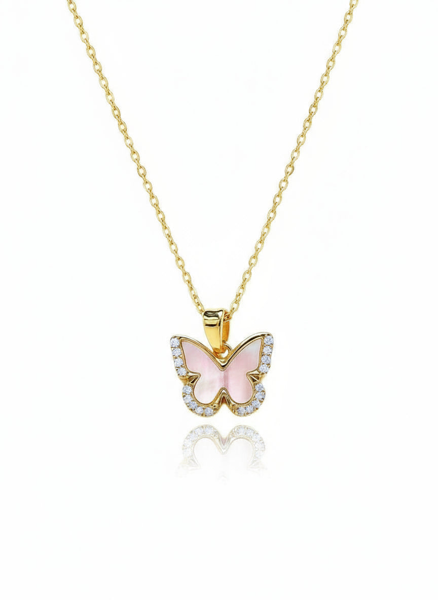 A gold-filled butterfly necklace with a white pearl in the center, displayed on a reflective surface.