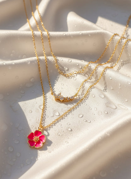 Gold necklace with a pink flower pendant on a textured beige surface