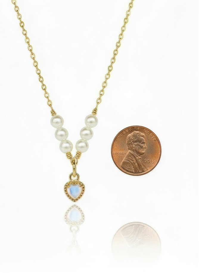 Necklace with pearl and gemstone pendant next to a penny on a white background