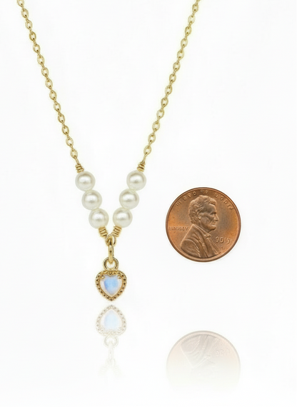 Necklace with pearl and gemstone pendant next to a penny on a white background